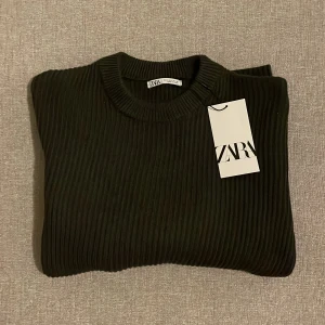 Svart ribbad tröja från Zara - Säljer en stilren svart ribbad tröja från Zara. Perfekt för både vardag och fest. Tröjan är i nytt skick med etikett kvar och har långa ärmar. Den är gjord i ett mjukt och bekvämt material som passar bra till höst och vinter.