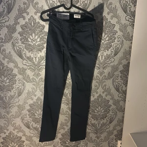 Mörkblå chinos från East West - Säljer ett par helt nya mörkblå chinos från East West i mycket bra skick. De har en slim passform och är perfekta för både vardag och fest. Materialet är stretchigt och bekvämt, vilket gör dem sköna att bära hela dagen. Passar perfekt till höst- och vårgarderoben!