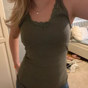 Olivgrön linnetopp från Noa Noa - Snygg olivgrön linnetopp från Noa Noa med spetsdetaljer vid halsringningen. Perfekt för sommardagar eller som ett lager under en kofta. Toppen är i bra skick och har en bekväm passform.