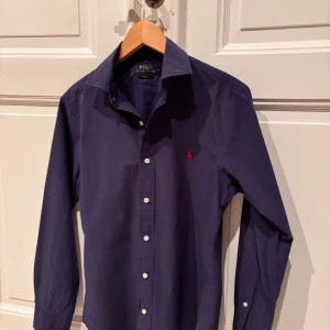 Mörkblå skjorta från Ralph Lauren - Säljer en stilren mörkblå skjorta från Ralph Lauren. Den är mörkblå och perfekt för vår/sommarn. Storlek är S, sitter lite mer som Xs. Nypris: 1695 kr