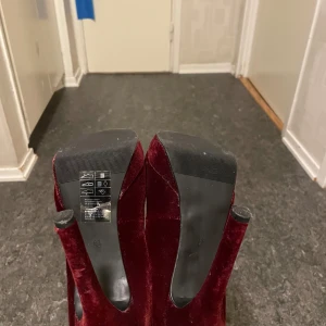 Vinröda sammetspumps från H&M - Säljer ett par eleganta vinröda pumps i sammet från H&M. De har en hög klack och en klassisk rund tå, perfekt för festliga tillfällen. Skorna är i mycket bra skick och ger en lyxig känsla med sitt mjuka material.