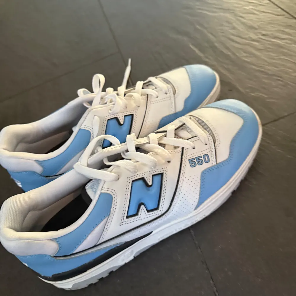 Säljer ett par New Balance 550 sneakers i snyggt blått och vitt. De har en klassisk design med snörning och är i mycket bra skick. Perfekta för både vardag och träning. Storlek 44, köpta på pardon my kicks. Pris kan diskuteras. Skor.