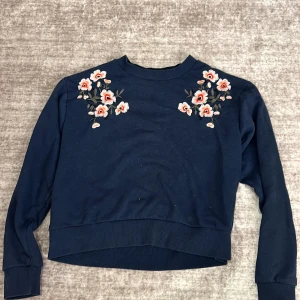 Mörkblå tröja med blommig broderi - Säljer en superfin mörkblå tröja från Madewell med vackra blommiga broderier på axlarna. Tröjan har långa ärmar och en bekväm passform, perfekt för både vardag och lite finare tillfällen. Den är i bra skick och redo för en ny ägare! 🌸