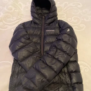 Svart dunjacka från Peak Performance - Säljer en svart dunjacka från Peak Performance i mycket bra skick. Jackan är perfekt för kalla dagar med sin pufferstil och långa ärmar. Den har en praktisk dragkedja och en mysig huva. Perfekt för både höst och vinter! ett 