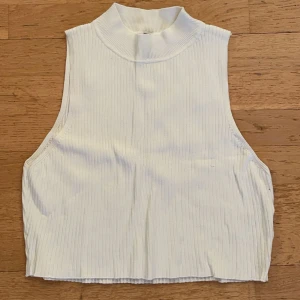 Vit ribbad linne - Säljer en stilren vit ribbad topp med hög krage. Den är ärmlös och perfekt för lager-på-lager eller att bära som den är under varmare dagar.
