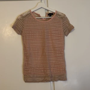 Beige/ ljus rosa spetsblus - Säljer en söt ljus rosa spetsblus med korta ärmar. Perfekt för sommardagar eller en festlig kväll. Blusen har ett fint mönster och är lätt och luftig. Passar bra till både jeans och kjol!