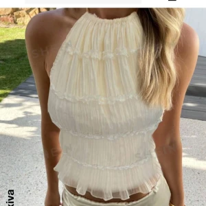 Krämfärgad halterneck topp - Snygg krämfärgad halterneck topp från SHEIN med volangdetaljer. Toppen är ärmlös och har en öppen rygg med knytband. Perfekt för sommarens fester eller en dag på stranden. Ej använd💗💗