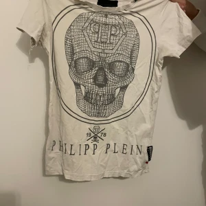Vit t-shirt från Philipp Plein - Säljer en  vit t-shirt från Philipp Plein med ett stort dödskalletryck på framsidan. T-shirten är i normal passform och har korta ärmar. Märkeslogga syns både fram och bak. Kontakta för fler bilder, lägre pris vid direkt köp