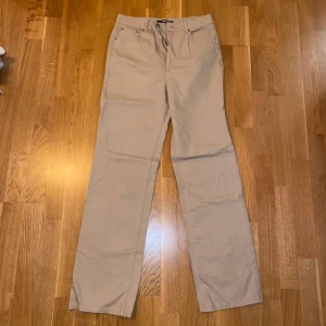 Beige byxor - Säljer ett par snygga beige byxor i bra skick. De har en klassisk straight passform och är perfekta för både vardag och lite mer uppklädda tillfällen. Byxorna är midwaist och har en enkel design med knappar och dragkedja framtill. Perfekta för höst och vår!