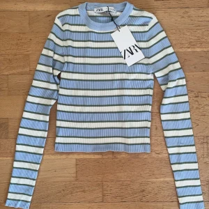 Randig ribbad tröja från Zara - Säljer en superfin och populär randig tröja från Zara i ljusblått, vitt och grönt. Den är ribbad och har en croppad passform som är perfekt för både vår och sommar. Tröjan har långa ärmar och är i nytt skick med lappen kvar. 