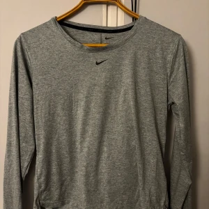 Grå långärmad tröja från Nike - Säljer en grå långärmad tröja från Nike i Dri-Fit material. Perfekt för träning eller vardagsbruk. Tröjan är i mycket bra skick och har en liten Nike-logga på bröstet. Superbekväm och andas bra!