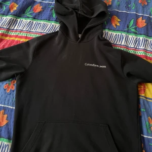 Svart hoodie från Calvin Klein Jeans - Säljer en stilren svart hoodie från Calvin Klein Jeans. Den har en klassisk design med en känguruficka och en liten logga på bröstet. Perfekt för både vardag och chill. Passar till allt och är superbekväm!