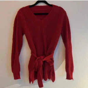 Röd stickad tröja med knytband - Säljer en superfin röd stickad tröja med v-ringning och ett snyggt knytband i midjan. Perfekt för höst och vinter, den är både varm och stilren. Tröjan har långa ärmar och en ribbad struktur som ger en skön passform. Passar perfekt till både vardag och fest! Storlek S