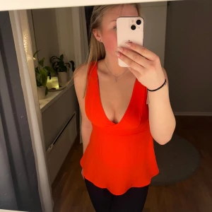 Röd ärmlös topp med knyt - Säljer en superfin röd ärmlös topp med v-ringning och en söt knytning i ryggen. Perfekt för sommardagar eller en utekväll. Toppen har en lös passform som ger en skön och luftig känsla.