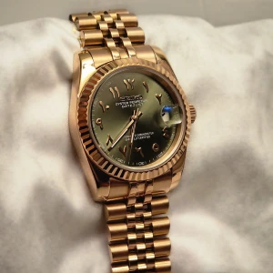 Seiko Mod - Arabisk Urtavla - Rosa Guld och Mörk Grön  - -Storlek: 36 mm -Urtavla: Grön med arabiska siffror -Glas: Safirglas med förstorad datumvisning -Baksida: Öppen baksida (transparent bakboett) -Visning: Självlysande visare i grön färg -Armband: Jubilee-armband i borstat stål -Urverk: Automatiskt Seiko NH35 med 41 timmars gångreserv -Förpackning: Levereras i en elegant klockfodral