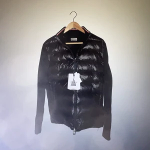 Moncler Cardigan - Säljer en snygg svart cardigan från Moncler. Denna cardigan är inte så vanlig och svår att få tag på den har en stilren design med dragkedja framtill och långa ärmar. Perfekt för höst och vinter, håller dig varm och trendig. Passar både till vardags och festliga tillfällen. Skriv vid frågor eller fler bilder!!