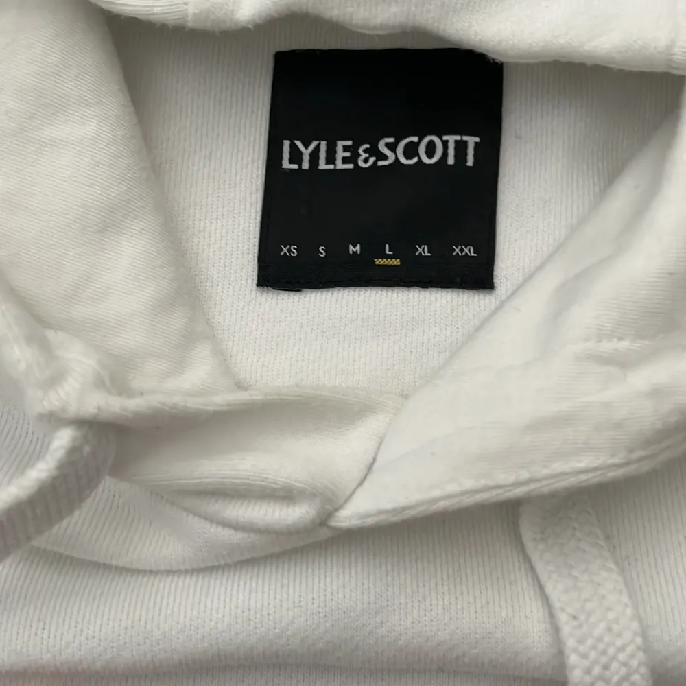 Säljer en stilren vit hoodie från Lyle & Scott. Den har en klassisk design med en liten gul logga på bröstet. Perfekt för en avslappnad look. Hoodien har en känguruficka och justerbar huva med dragsko.. Tröjor & Koftor.