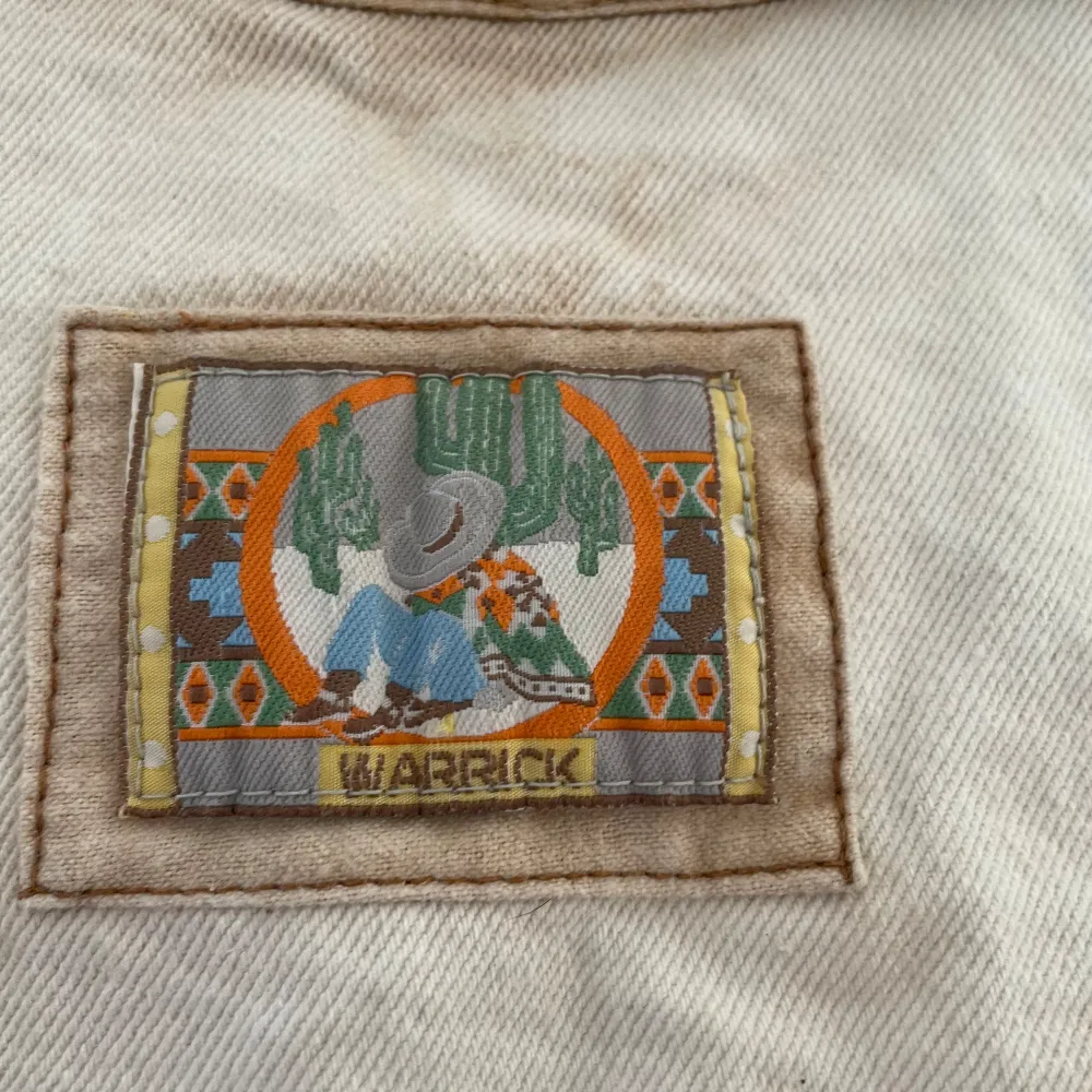 Säljer en vintage vit jeansjacka från Warrick, tillverkad i Finland. Jackan har en klassisk design med knappar framtill och flera fickor. Den har en cool patch på ryggen med ett unikt mönster. Perfekt för vår och sommar!. Takit.