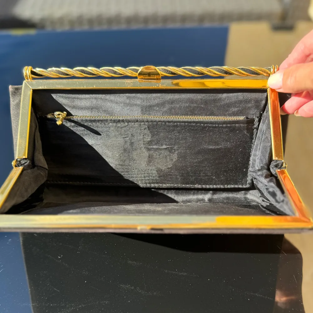 Svart kuvertväska / clutch. Väskan har guldfärgad ram och en vriden gulddetalj upptill. Insidan är fodrad med ett fack med dragkedja. Perfekt för en kväll ute eller en speciell tillställning! Mått -se linjal. Hämtas på Hägerstensåsen eller ök 🖤. Laukut & Käsilaukut.