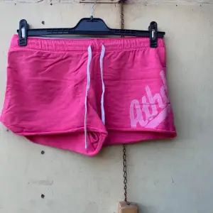 Säljer ett par snygga rosa shorts från Nike. De är perfekta för träning eller en avslappnad dag. Shortsen har en bekväm passform med snörning i midjan och en cool logga på sidan. Materialet känns mjukt och skönt mot huden.