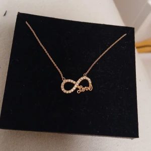 Guldhalsband med infinity-symbol och texten 'Love' - Jag cill sälja detta rosa halsband som jag köpte för 400kr men de blev till ingen avändning så tänkte sälja den för 200kr.