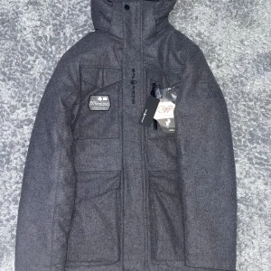 Sail Racing Glacier Bay Wool Parka - En helt ny och oanvänd Sail Racing Glacier Bay Wool Parka. Det är en tjock vinterjacka i samma material som en kappa. Storlek: Small. Färg: Mörkgrå. Skick: Helt ny.