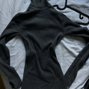 Mörkgrå ribbad polotröja från Gina Tricot - Säljer en snygg och stilren mörkgrå polotröja från Gina Tricot. Den är ribbad och har långa ärmar, perfekt för höst och vinter. Tröjan är i storlek XS och passar perfekt för en chic och bekväm look. Perfekt för både vardag och fest!