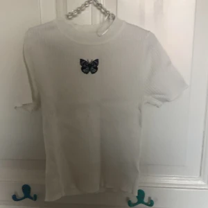 Vit tröja - En vit tröja med en fjäril på, storlek XS men går att stretcha ut rätt så mycket. Tröjan är i bra form och har inga hål i sig 