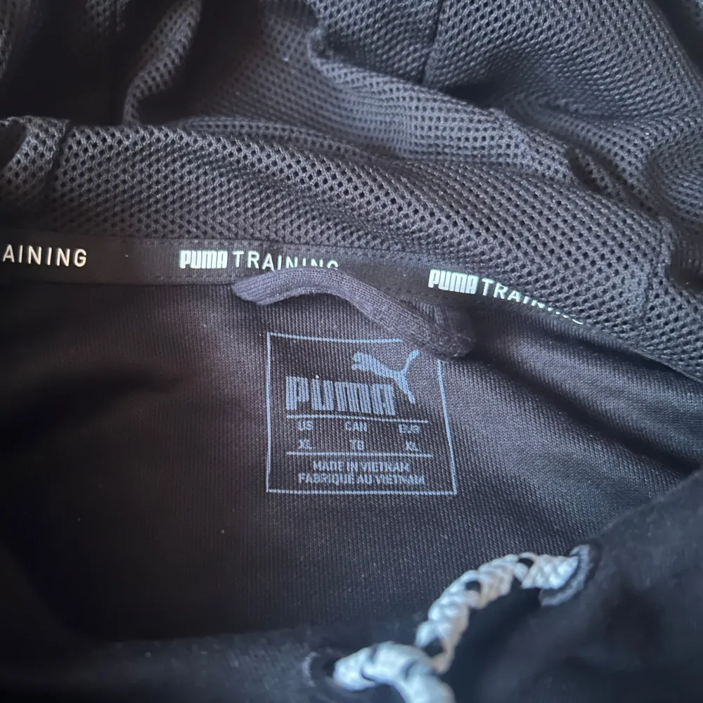 Säljer en svart hoodie från Puma med stort logotryck i vitt på framsidan. Tröjan har långa ärmar och en justerbar huva med snören. Perfekt för träning eller en avslappnad stil.. Neuletakit & Villapaidat.
