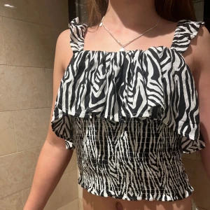 Zebramönstrad topp med volang - Snygg zebramönstrad topp med volangdetaljer och smockad nederdel. Axelbanden är volangprydda och ger en extra touch. Perfekt för en trendig look.