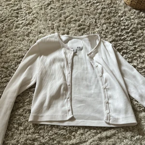 Vit ribbad kofta från 157 - Säljer en stilren vit ribbad kofta från 157. Koftan har långa ärmar och knappar framtill. Perfekt för lager-på-lager och passar till många olika outfits. 🖤passar även xs kan dock bli lite kort i armen. 