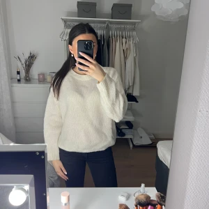 Vit stickad tröja - Mysig vit stickad tröja med långa ärmar och rund hals. Perfekt för kyligare dagar och enkel att matcha med olika outfits. Tröjan har en klassisk design med ribbade kanter vid ärmslut och nederkant.