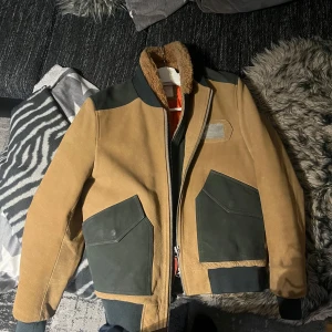 Beige och grön jacka från Scotch & Soda - Säljer en snygg beige och grön jacka från Scotch & Soda. Jackan har en dragkedja och en mysig pälsliknande krage. Den har långa ärmar och praktiska fickor framtill. Perfekt för kyligare dagar! Bara användt ett par gånger! Kontakta gärna innan och lägg bud!🥰🥰