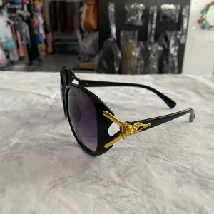 Snygg Dam Solglasögon med gulddetaljer - Snygga solglasögon med stora runda linser och gulddetaljer vid skalmarna. Finns i flera färger: svart, brun, röd och lila. Perfekta för att ge en glamorös touch till din stil. 149kr/st helt ny 