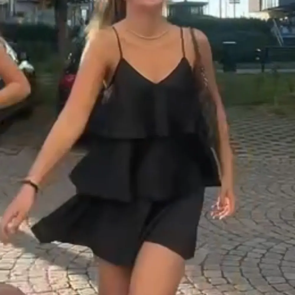 Snygg svart klänning med smala axelband och volangdetaljer. Perfekt för en stilren look. Klänningen har en luftig passform och är tillverkad i ett lätt material som ger ett fint fall.. Mekot.