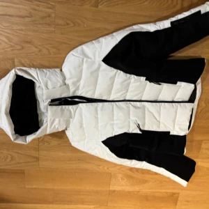 Vit och svart pufferjacka från Everest - Säljer en snygg ny vit och svart pufferjacka från Everest. Jackan har en dragkedja framtill och en praktisk huva. Perfekt för kyliga dagar med sin stilrena design och bekväma passform.