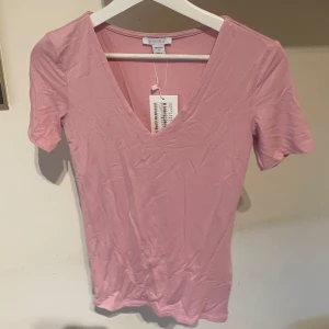 Rosa v-ringad topp - Säljer en söt rosa v-ringad topp. Toppen har korta ärmar och är perfekt för en avslappnad stil. Den är gjord i ett mjukt material som känns skönt mot huden.