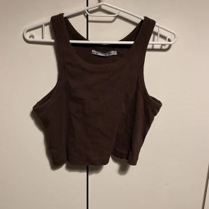 Brun ribbad linnetopp - Säljer en brun ribbad linnetopp från Lager 157. Toppen är ärmlös och har en croppad passform, perfekt för varmare dagar. Den är enkel och stilren, vilket gör den lätt att matcha med olika outfits.