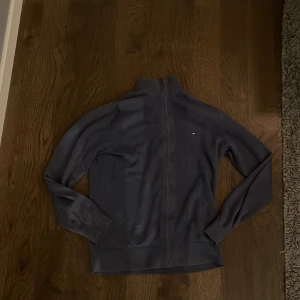 Blå Kashmir blandad tröja från Tommy Hilfiger - Säljer en blå kashmirblandad tröja  från Tommy Hilfiger med dragkedja och liten logotyp på bröstet.  Den är tillverkad i en mjuk och bekväm materialblandning med kashmir. Riktigt fettt!😁 säljs pga lite kort på mig. Pris är ej hugget i sten 