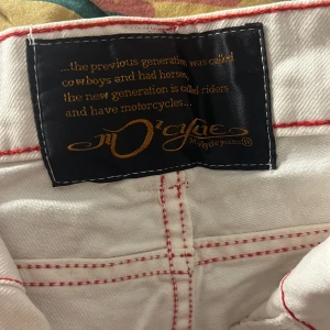Vita byxor med röda sömmar från Cycle - Snygga vita byxor från Cycle med kontrasterande röda sömmar. De har en klassisk femficksdesign och en knappgylf. Perfekta för en stilren look.