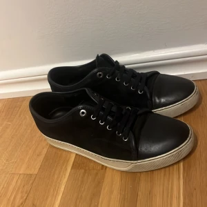 Mörk blå  sneakers från Lanvin - Snygga svarta sneakers från Lanvin med vita sulor och klassisk snörning. Skorna har en stilren design med svarta skosnören och metallöljetter. Perfekta för en avslappnad men stilfull look.mrn tyvär är inte boxen med men dom är riktiga. Storklek uk 7