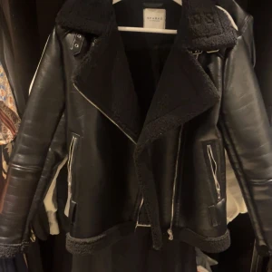Svart skinnjacka från Sparkz Copenhagen - Snygg svart skinnjacka från Sparkz Copenhagen med fuskpälsdetaljer på krage och ärmslut. Jackan har dragkedja och två fickor med dragkedjor. Perfekt för en cool look! Finns inget bälte till!!!