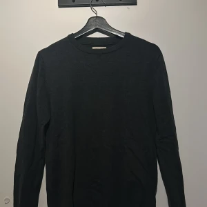 Mörkgrå tröja från Jack & Jones - Säljer en stilren svart tröja från Jack & Jones. Tröjan har en klassisk rund hals och långa ärmar, perfekt för en enkel och snygg look. Passar bra till både jeans och chinos.