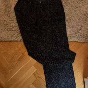 Svarta leopardmönstrade byxor - Snygga svarta byxor med leopardmönster. De har en loose passform och är lågmidjade, vilket ger en bekväm och trendig look. Perfekta för att sticka ut med stil. Använda två gånger. Passar M/L