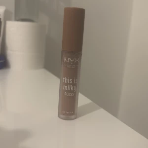 Brun läppglans från NYX - Säljer ett NYX 'This is Milky' läppglans i en mjuk brun nyans. Perfekt för en naturlig look med en glansig finish. Kommer i en praktisk tub med applikator för enkel applicering.