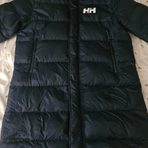 Blå dunjacka från Helly Hansen - Säljer en blå lång dunjacka från Helly Hansen med dragkedja och två praktiska fickor framtill. Jackan har en quiltad design och är perfekt för kalla dagar. Helly Hansen-loggan syns både fram och bak. Nypris 6.500kr. Köpt i Oslo! Använt sporadiskt.