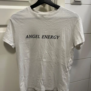 Vit t-shirt med texten 'Angel Energy' - Vit t-shirt med texten 'Angel Energy' tryckt på framsidan. Den har en klassisk rund hals och korta ärmar. Perfekt för en avslappnad stil.