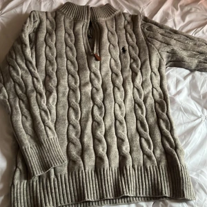 Beige kabelstickad tröja från Ralph Lauren - Säljer en stilren beige kabelstickad tröja från Ralph Lauren med dragkedja och ribbade detaljer vid krage, ärmslut och nederkant. Perfekt för kyligare dagar och ger en klassisk look. 🧥Passar M,L och XL