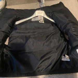 Svart dunväst med dragkedja - Snygg svart dunväst med dragkedja framtill. Perfekt för kyligare dagar och ger en stilren look. Västen har en quiltad design som ger extra värme och komfort.