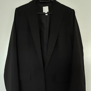 Kavaj, H&M, M, svart - Svart kavaj från H&M i nyskick, storlek M. 100% polyester. Skulle säga den är oversized modell.  Mått: Längd ca 76 cm Ärmlängd mätt från axeln ca 65 cm Ärmlängd axlar ca 65 cm